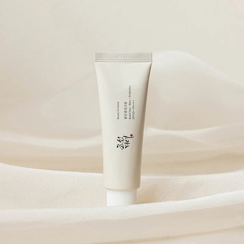 weiße Sonnencreme Tube steht elegant auf einem beigen, weichen drapierten Stoff.