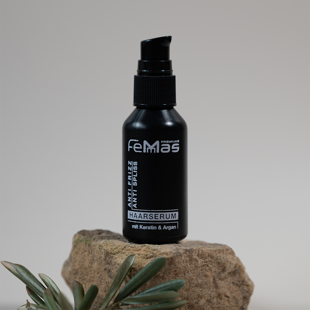 Schwarze FemMas Haarserum-Flasche auf einem Stein platziert, dekoriert mit grünen Blättern.