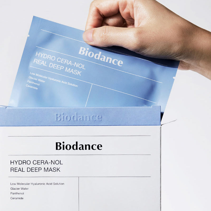 Eine Hand zieht eine Biodance Hydro Cera-Nol Real Deep Maske aus einer weißen Verpackung.
