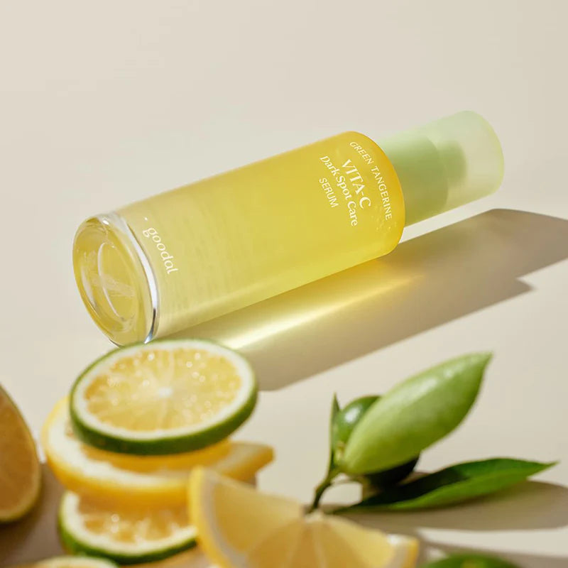 Flasche des Vita-C Serums liegt auf hellem Untergrund, umgeben von aufgeschnittenen Zitronen.