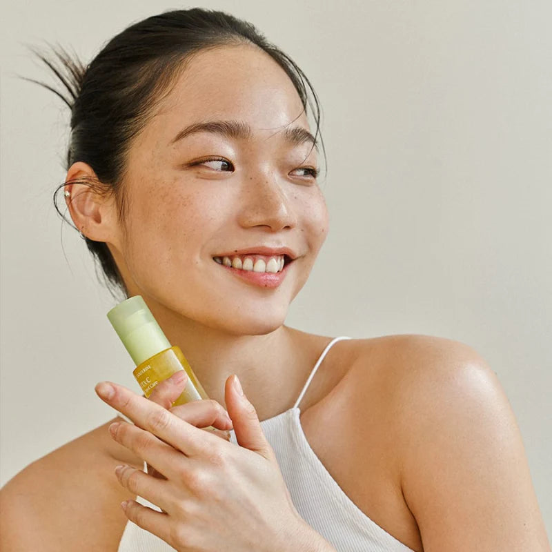 Lächelnde Frau hält das Gelb-transparente Vita-C Serum in der Hand.