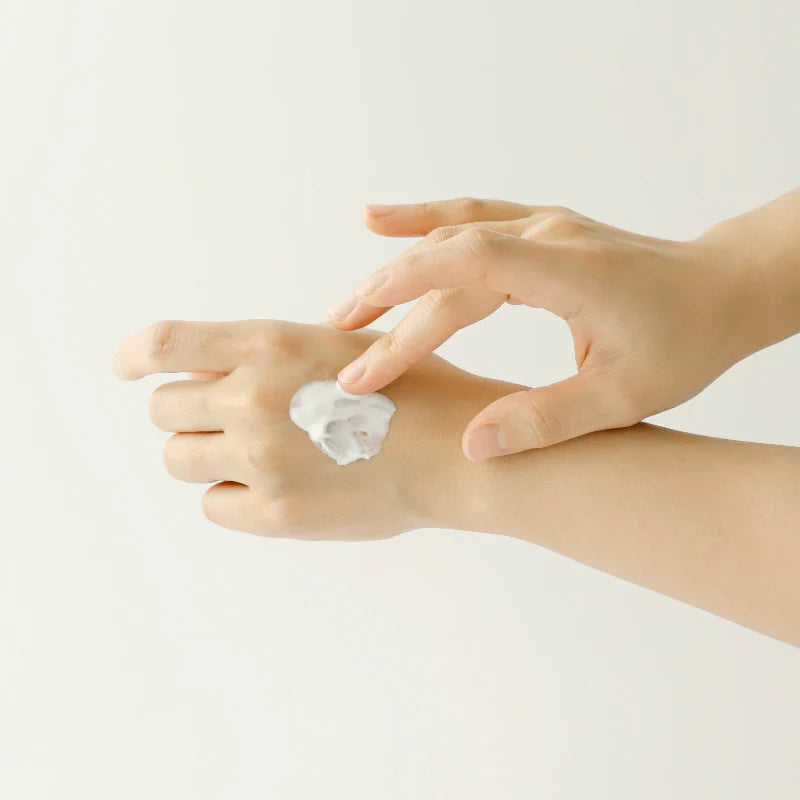 Zwei Hände, die eine weiße Creme auf dem Handrücken verteilen.