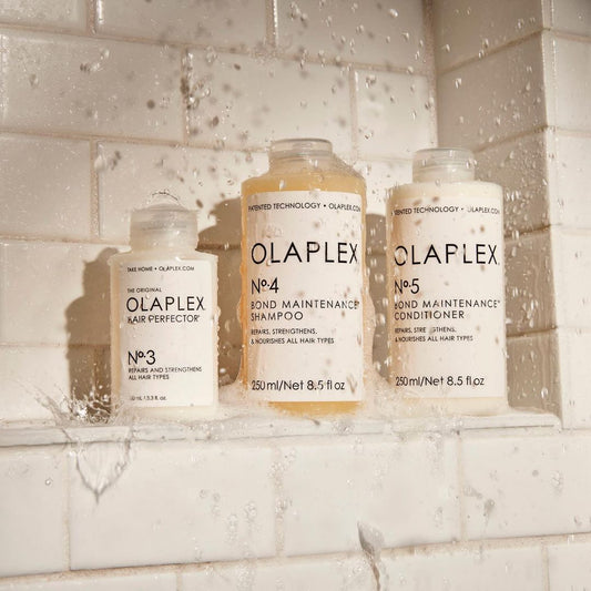 Die Produkte stehen in einer Dusche auf weißem Fliesenhintergrund, mit Wasser und Tropfen, die Frische und Anwendung während der Haarwäsche betonen.