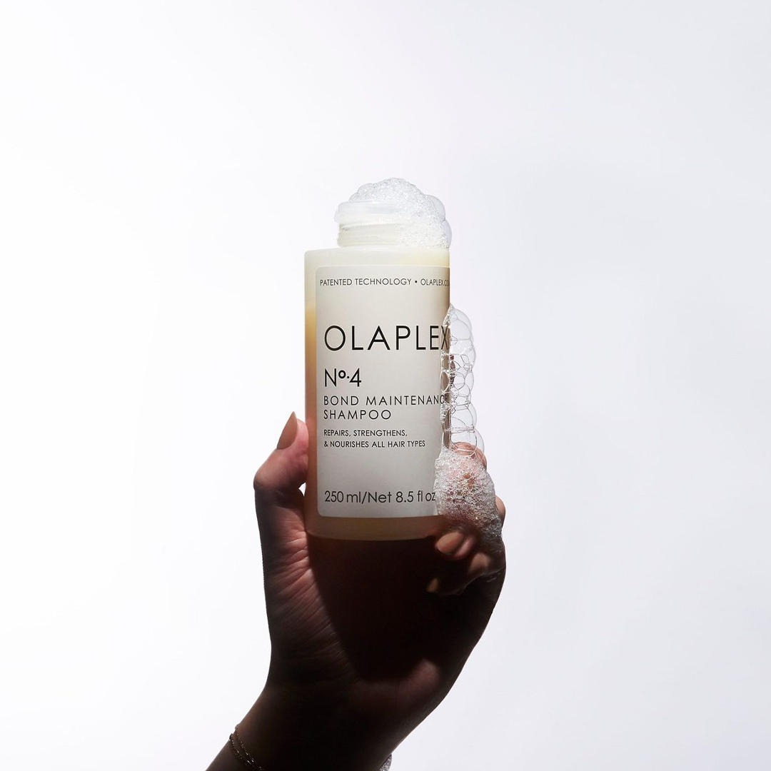 Hand hält die Olaplex No. 4 Shampoo-Flasche, Schaum fließt heraus.