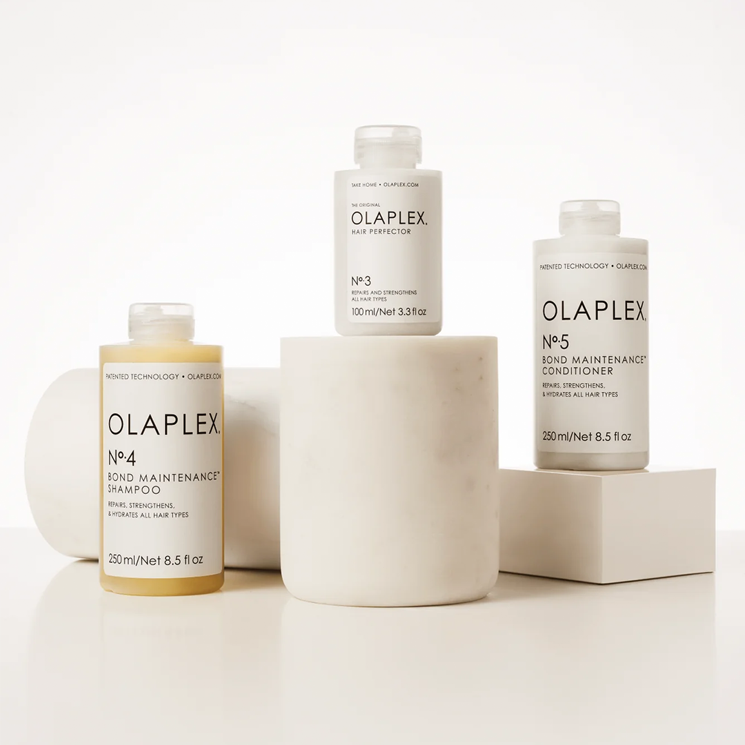 Drei Olaplex Produkte arrangiert auf weißen Zylindern. Hintergrund minimalistisch in hellen Tönen.
