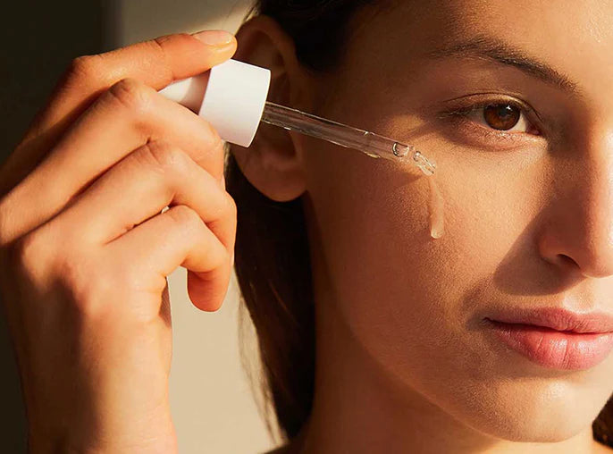 Eine Frau trägt mit der Pipette die Ampoule auf ihre Wange auf.