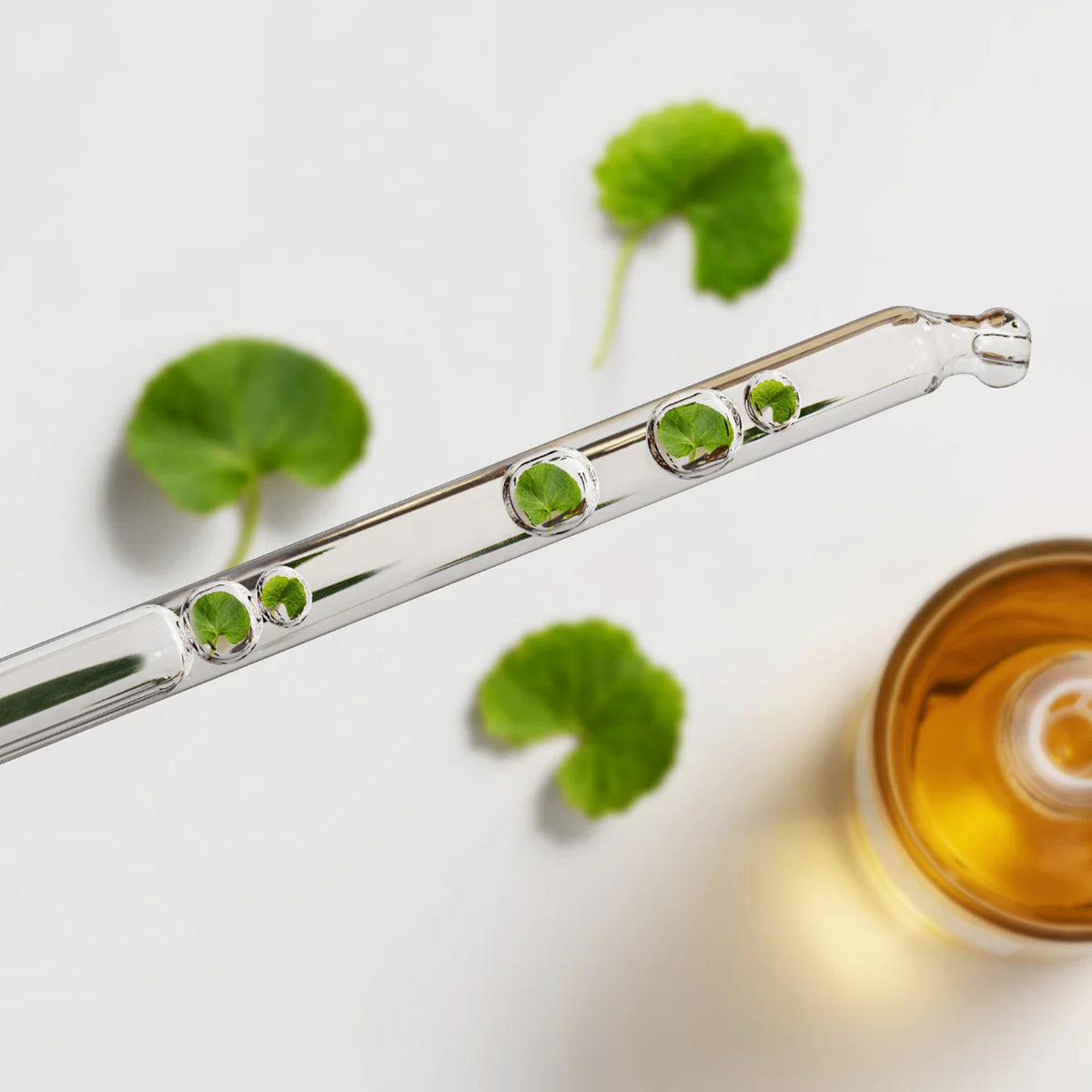 Eine Pipette mit Tropfen und kleinen grünen Blättern vor unscharfem Hintergrund.