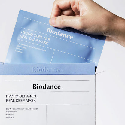 Eine Hand zieht eine Biodance Hydro Cera-Nol Real Deep Maske aus einer weißen Verpackung.