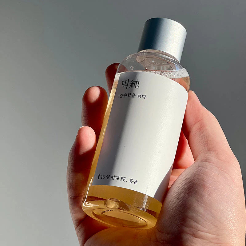 Hand hält die transparente Flasche mit Etikett und silbernem Verschluss.