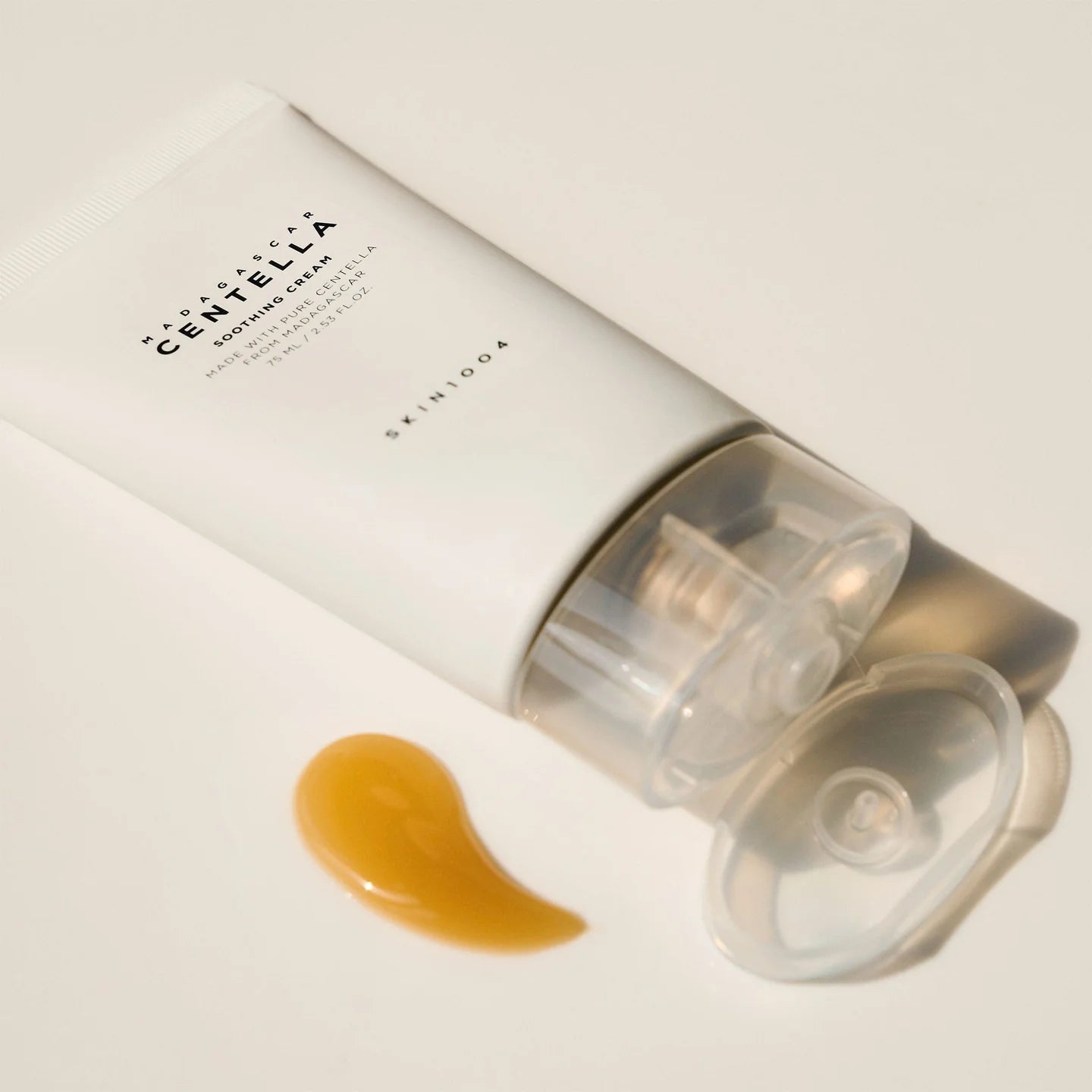 Nahaufnahme der Tube auf einer hellen Oberfläche, goldene Creme daneben.